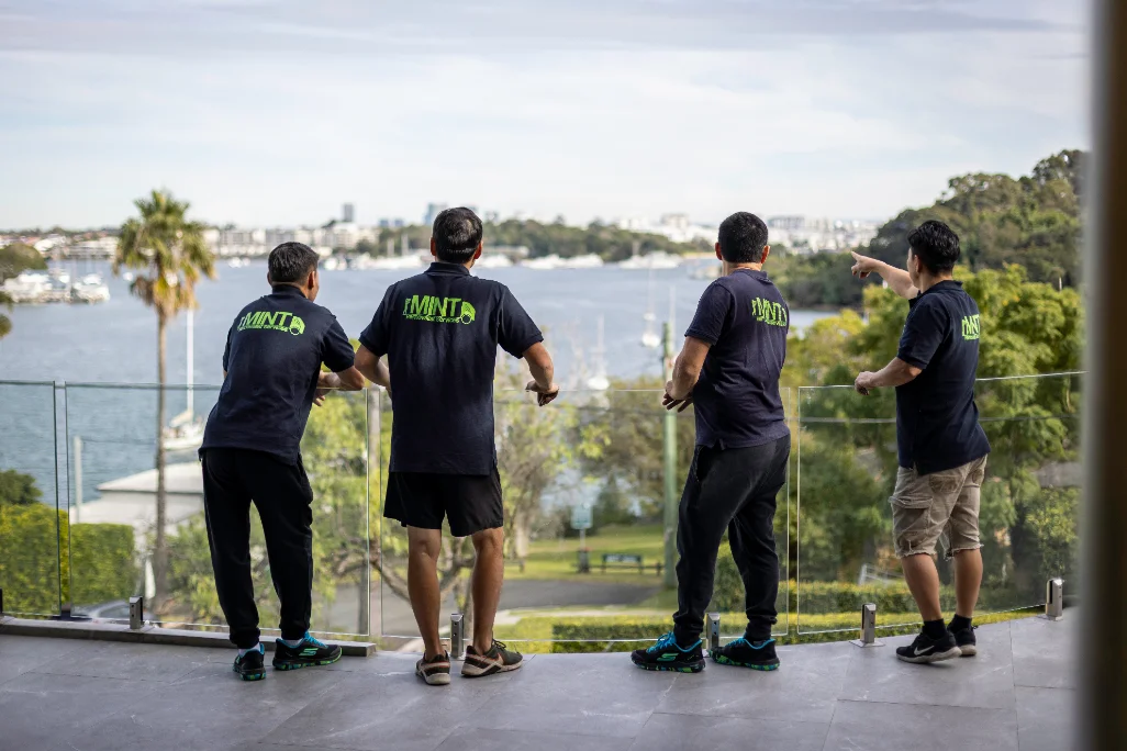 Four Mint Removals movers on a balcony overlooking Sydney Harbour