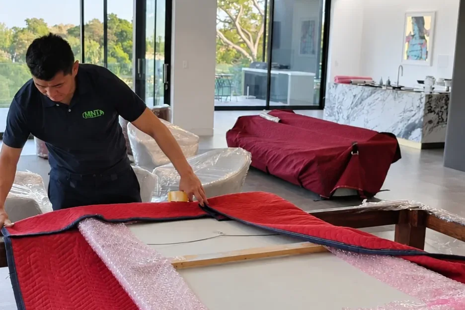 A Mint Removals mover folding a padded blanket over a bubble-wrapped framed artwork