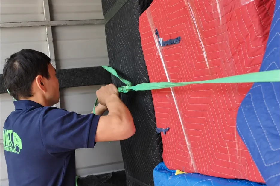A Mint Removals mover tying a strap across blanket-wrapped furniture inside a truck