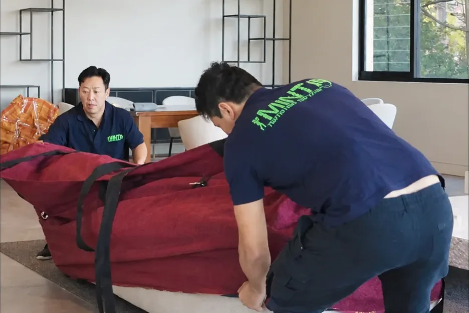 Two Mint Removals movers fitting a padded blanket and straps around a sofa