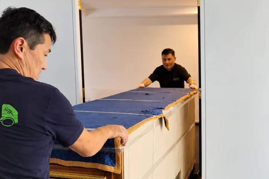Two Mint Removals movers guiding a large wrapped cabinet through a doorway
