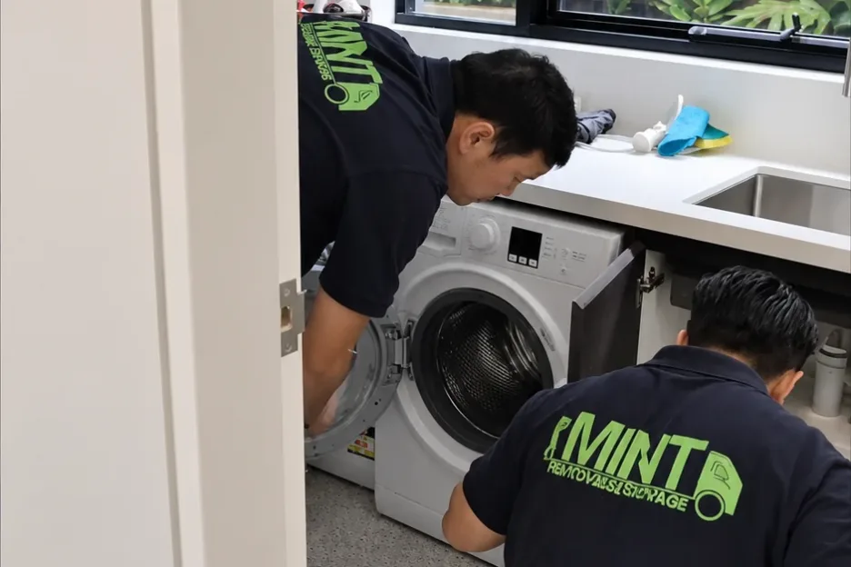 Two Mint Removals movers preparing a front-loading washing machine for the move