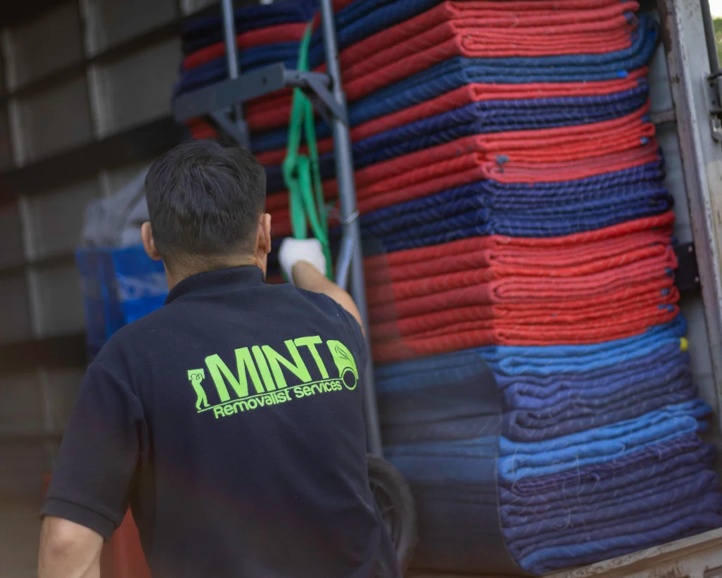 Stacked red and blue moving blankets beside a Mint Removals mover