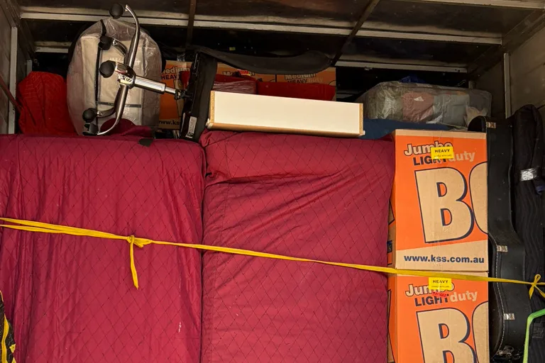 A removal truck loaded with blanket-wrapped furniture and boxes, strapped in place